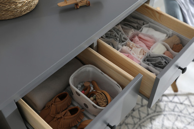 Photo of Open cabinet drawers with clothes and different items in child room