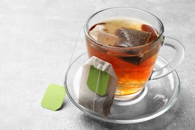 Photo of Tea bags and glass cup of hot beverage on light table, closeup. Space for text