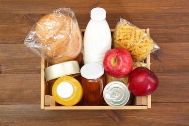 Photo of Humanitarian aid. Different food products for donation in crate on wooden table, top view