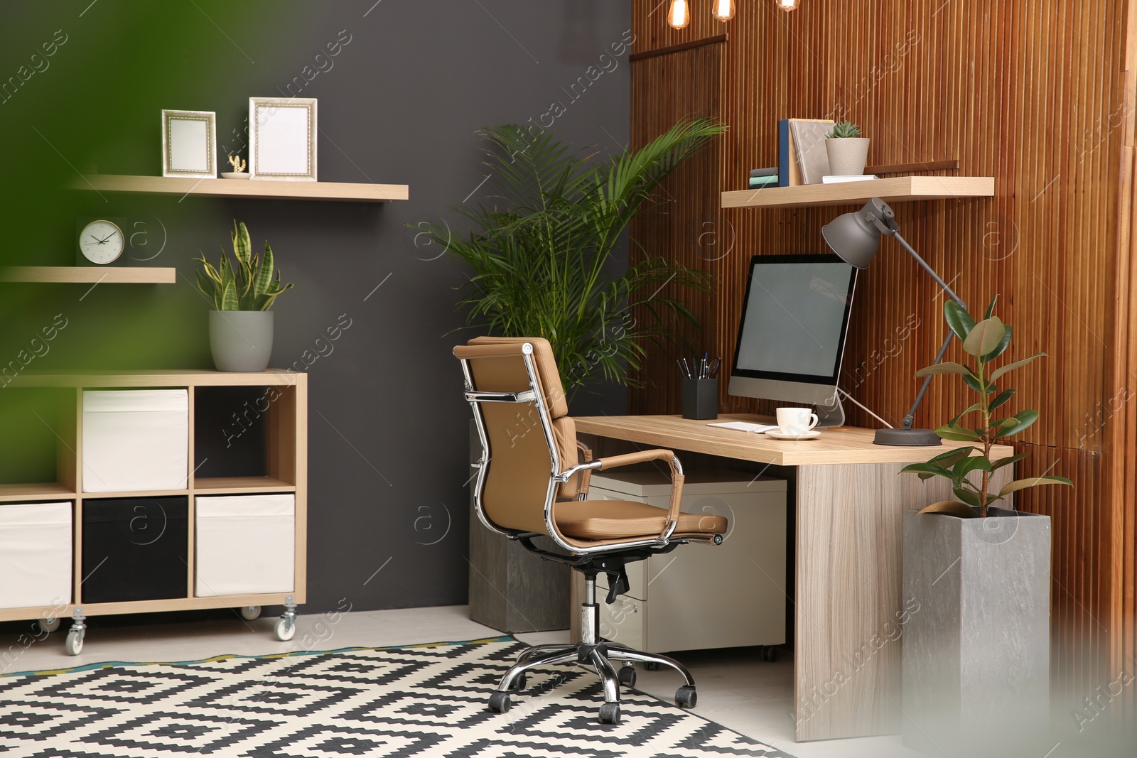 Photo of Comfortable workplace with computer near wooden wall in stylish room interior. Home office design