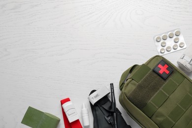 Military first aid kit, tourniquet, pills and elastic bandage on white wooden table, flat lay. Space for text