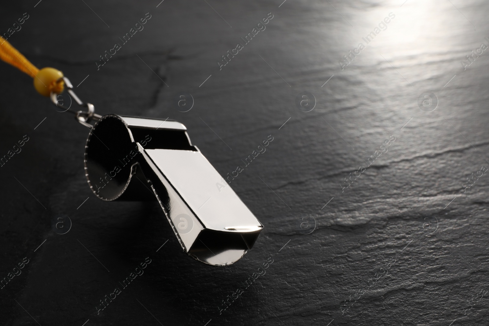 Photo of Referee equipment. Metal whistle on black textured background, closeup and space for text