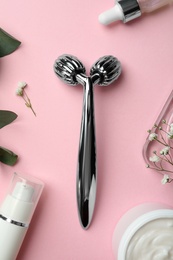 Photo of Metal face roller, cosmetic products and flowers on pink background, flat lay