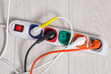 Photo of Power strip with different electrical plugs on white floor, flat lay