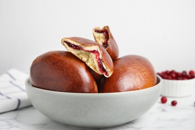 Photo of Delicious baked cranberry pirozhki in bowl on white marble table