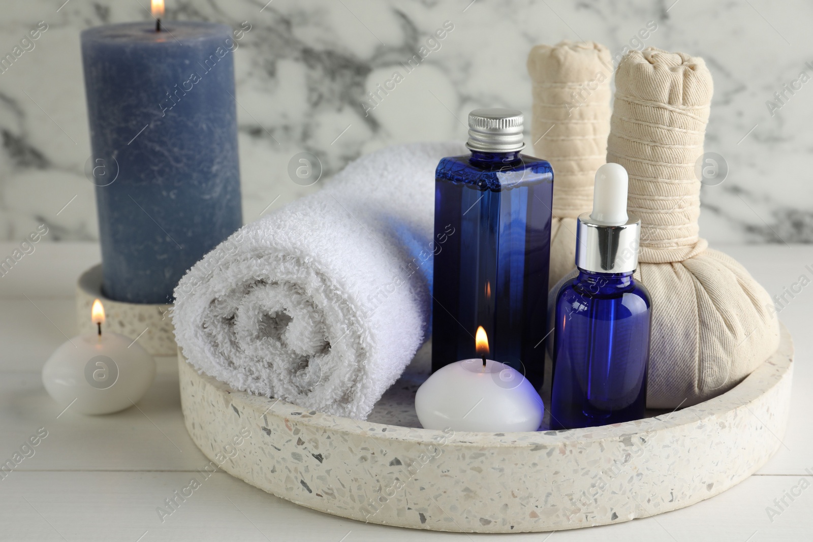 Photo of Spa composition. Bottles of cosmetic products, towel, herbal bags and burning candles on white wooden table