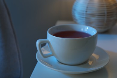 Photo of Cup of hot tea and nightlight on white table at night, closeup