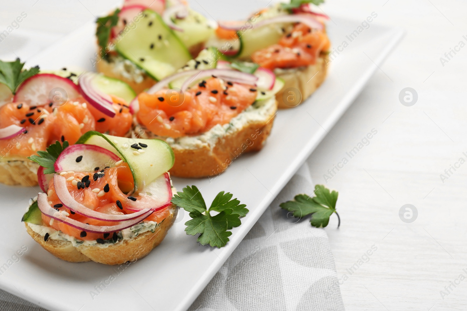 Photo of Tasty canapes with salmon served on white wooden table, closeup. Space for text