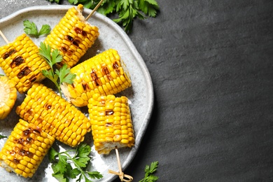 Delicious grilled corn cobs on grey table, flat lay. Space for text