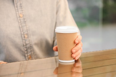 Photo of Woman holding takeaway paper cup at table, closeup. Coffee to go