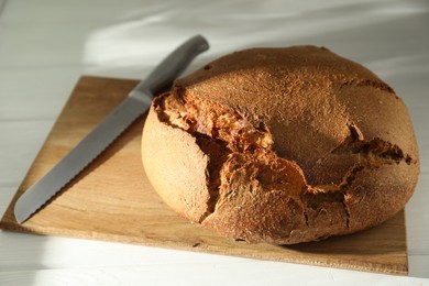 Photo of Freshly baked sourdough bread and knife on white table