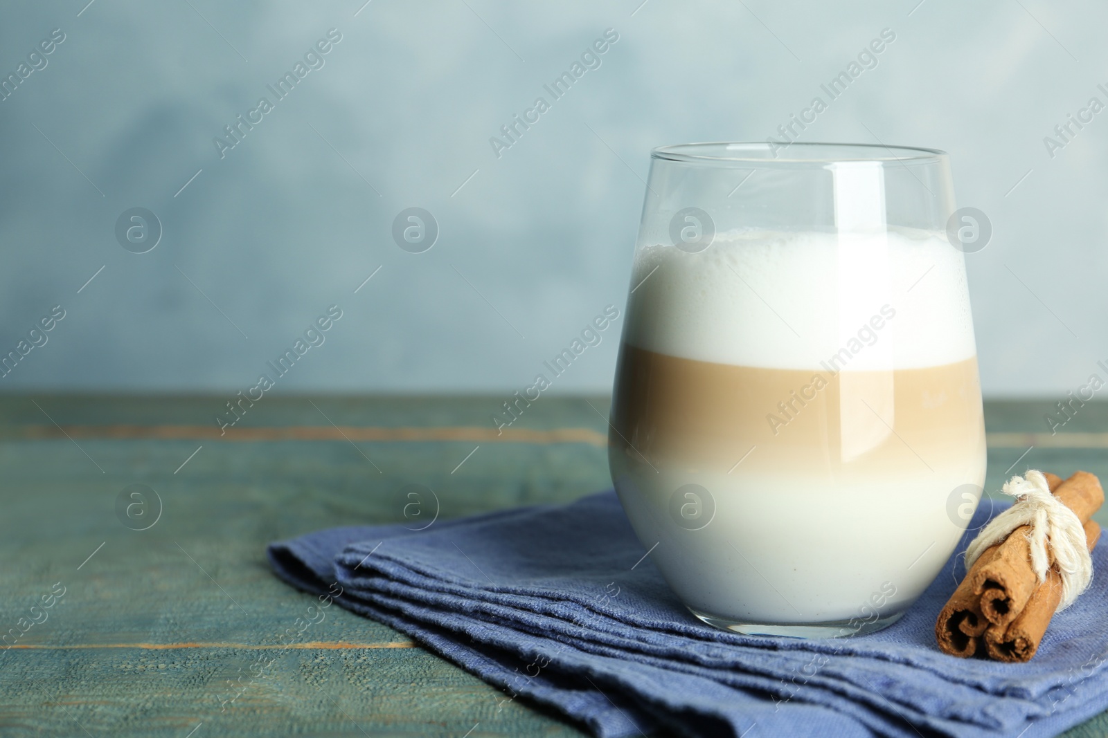 Photo of Delicious latte macchiato and cinnamon on wooden table against light blue background, space for text