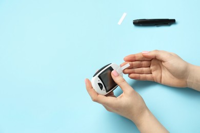 Photo of Diabetes. Woman checking blood sugar level with glucometer on light blue background, top view. Space for text