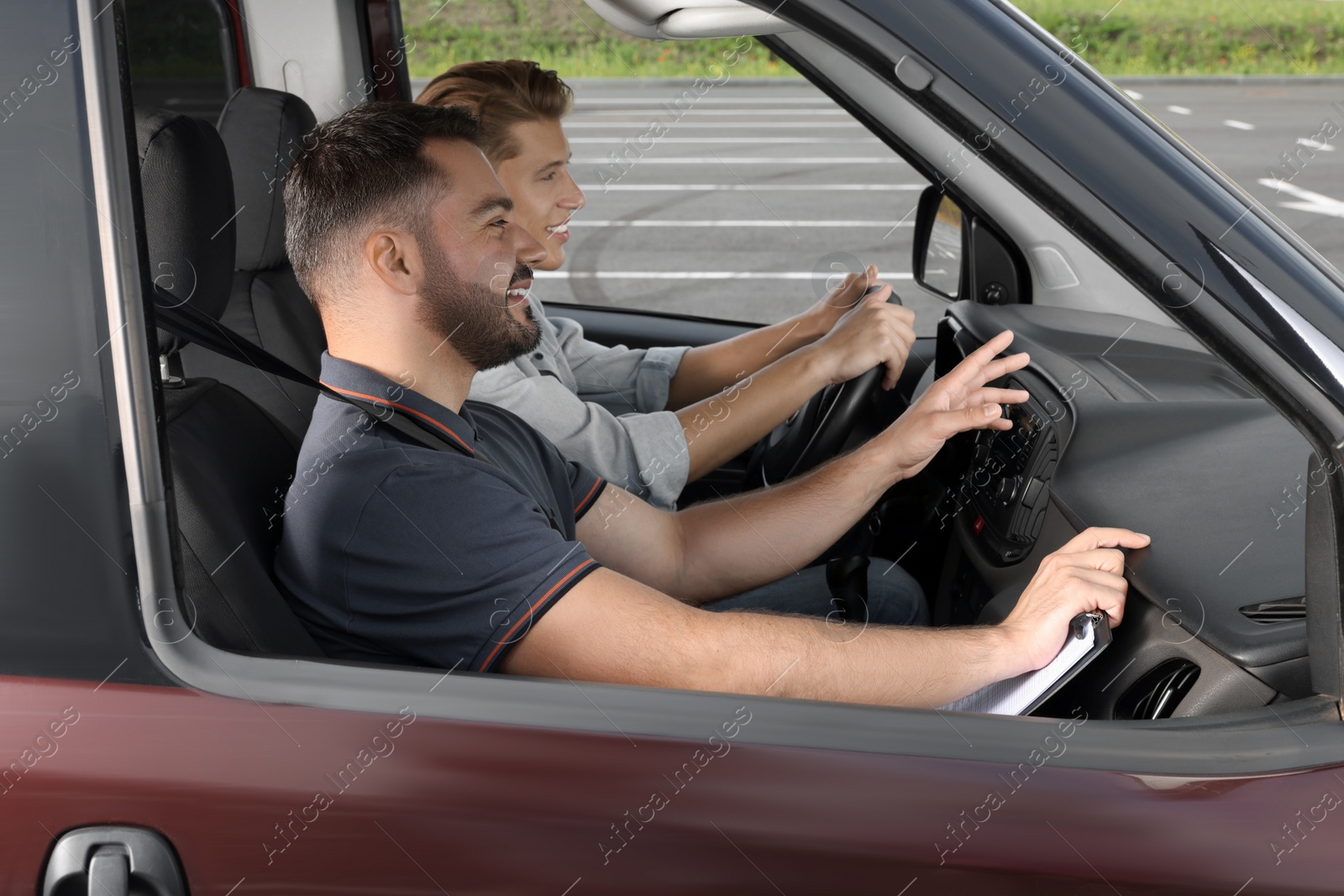 Photo of Driving school. Happy student passing driving test with examiner in car at parking lot