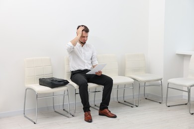 Man with sheet of paper waiting for job interview indoors