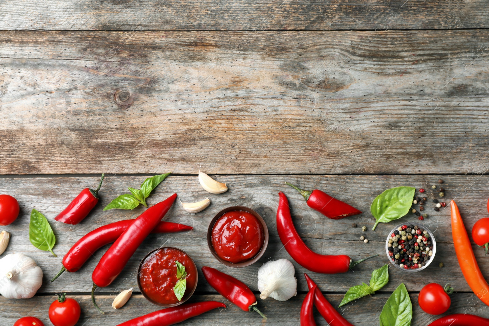 Photo of Flat lay composition with bowls of hot chili sauce and different spices on wooden background