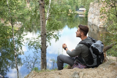 Young man with backpack sitting near lake. Camping season