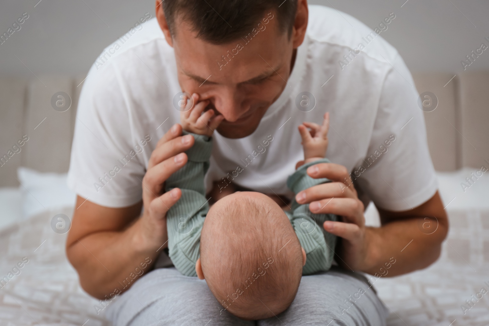 Photo of Happy father holding his cute baby on bed at home