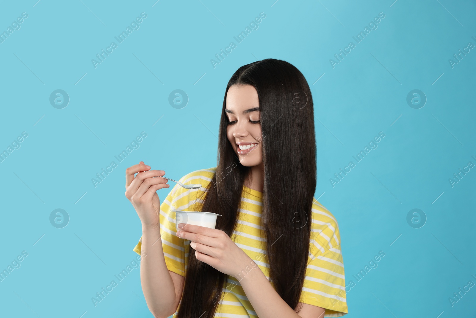 Photo of Happy teenage girl with delicious yogurt and spoon on light blue background