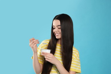 Happy teenage girl with delicious yogurt and spoon on light blue background
