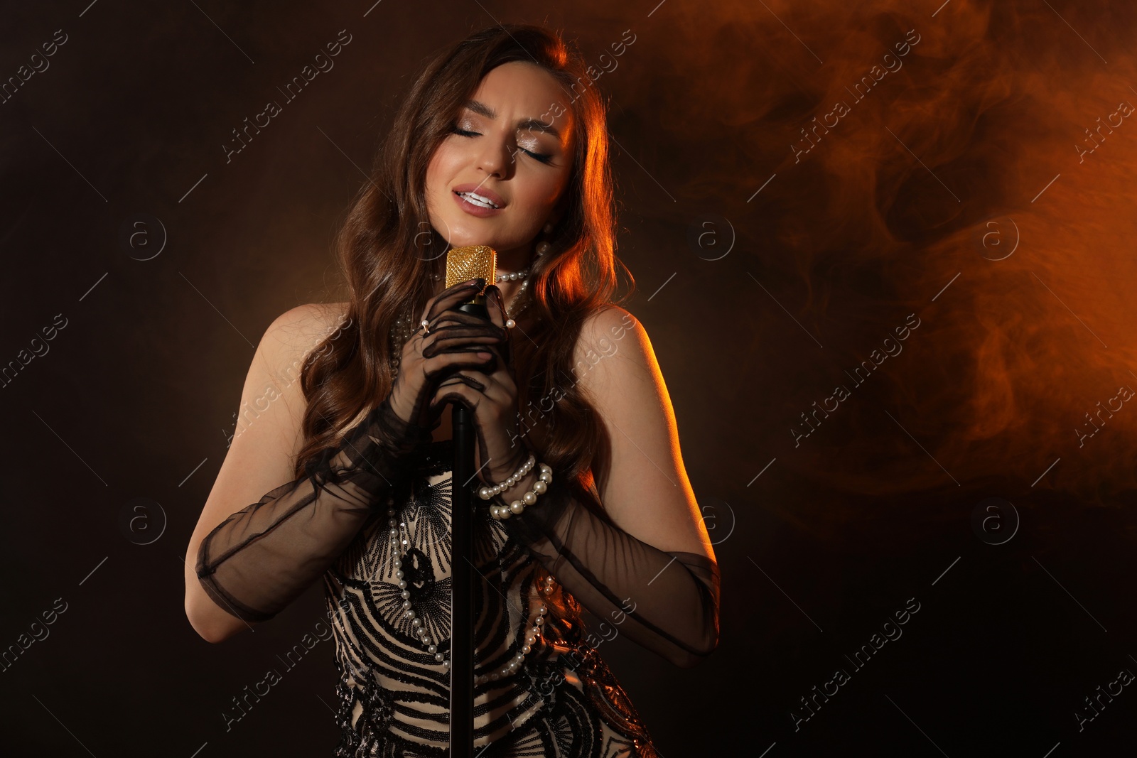 Photo of Beautiful young woman with microphone singing in color lights and smoke