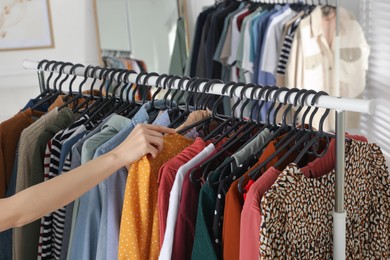 Woman picking clothes from rack indoors, closeup. Fast fashion