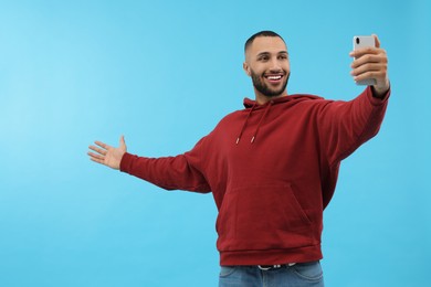 Photo of Smiling young man taking selfie with smartphone on light blue background