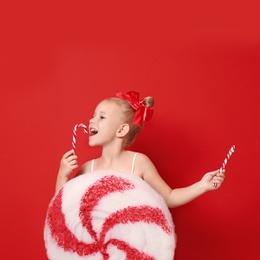 Cute little girl dressed as candy with sweets on red background. Christmas suit