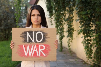 Photo of Sad woman holding poster with words No War outdoors. Space for text