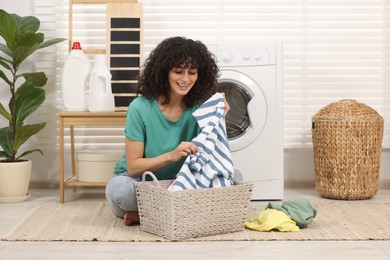 Photo of Happy woman with laundry near washing machine indoors