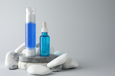 Photo of Bottles of cosmetic products and stones on light grey background. Space for text