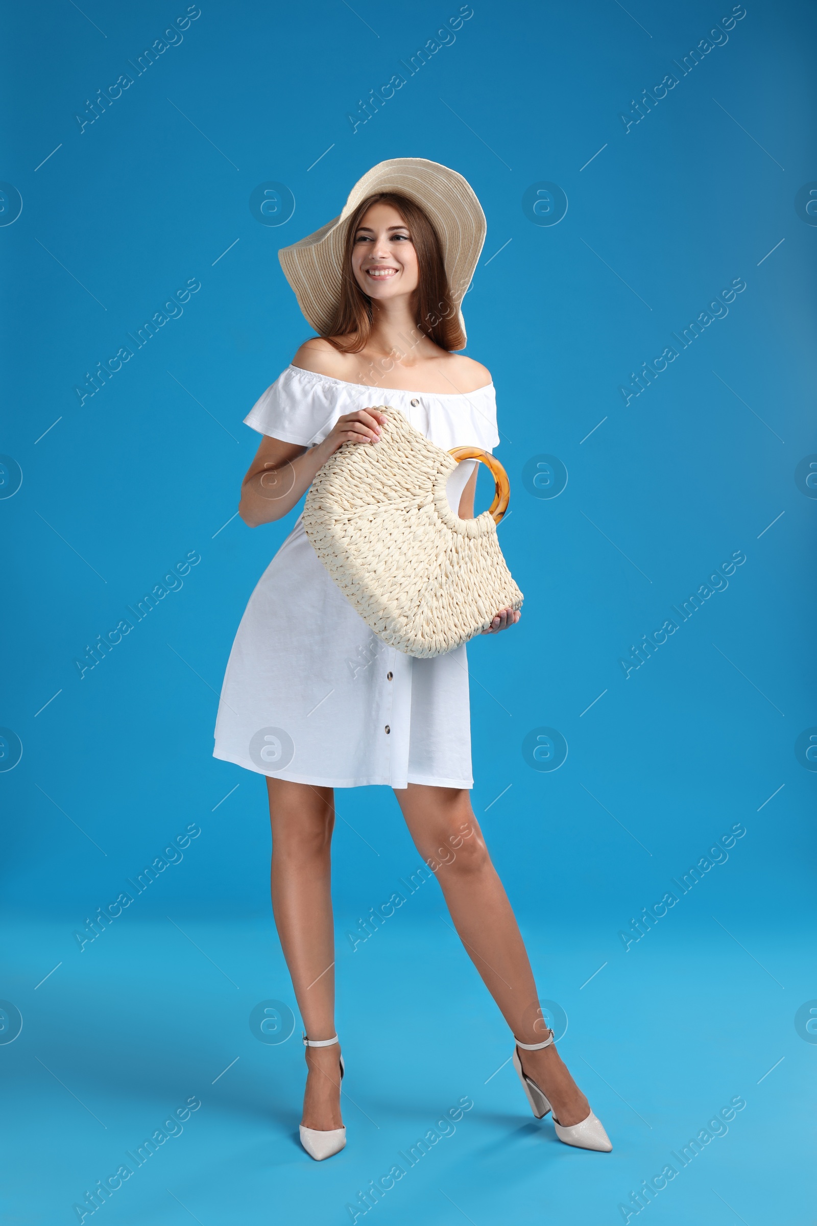 Photo of Beautiful young woman with stylish straw bag on light blue background