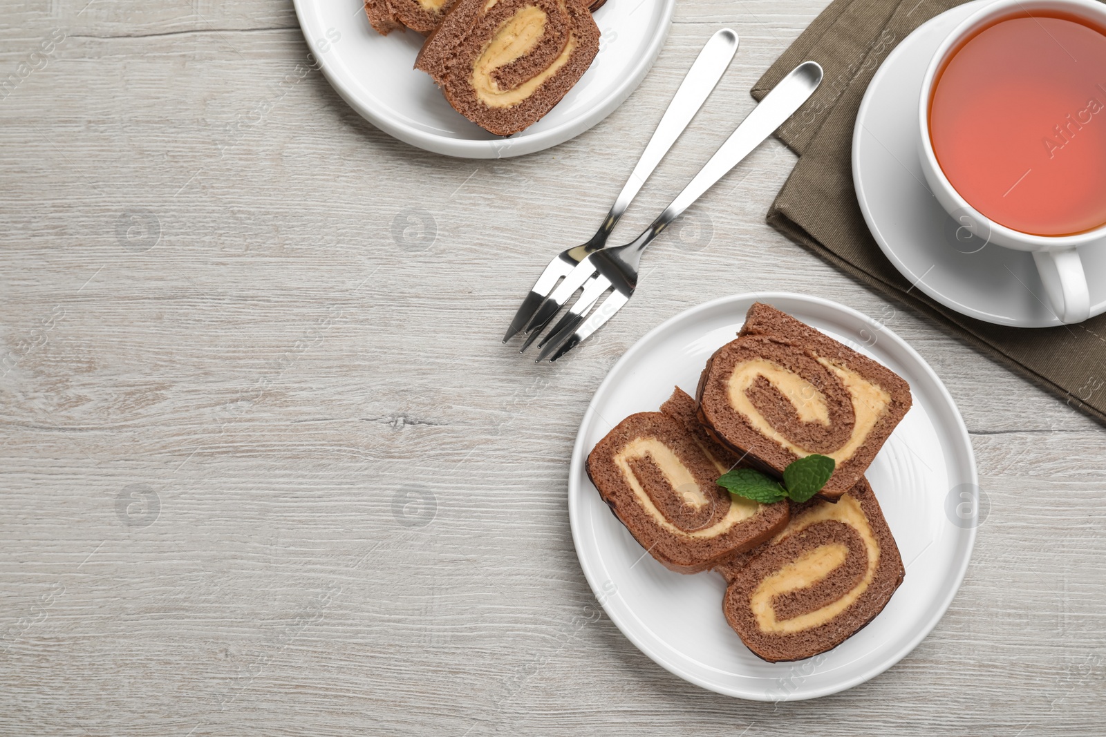 Photo of Tasty chocolate cake roll with cream and mint on light wooden table, flat lay. Space for text