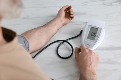 Photo of Man measuring blood pressure at white marble table, closeup