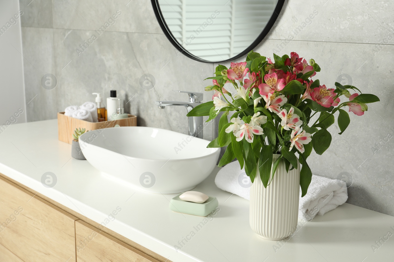 Photo of Vase with beautiful Alstroemeria flowers and toiletries near sink in bathroom