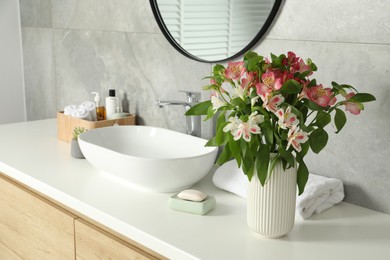 Photo of Vase with beautiful Alstroemeria flowers and toiletries near sink in bathroom