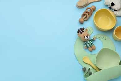 Flat lay composition with baby feeding accessories and bib on light blue background, space for text