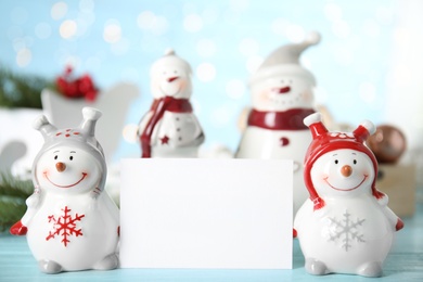 Decorative snowmen near blank white card on light blue table, space for text