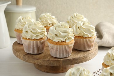 Photo of Tasty vanilla cupcakes with cream on white wooden table