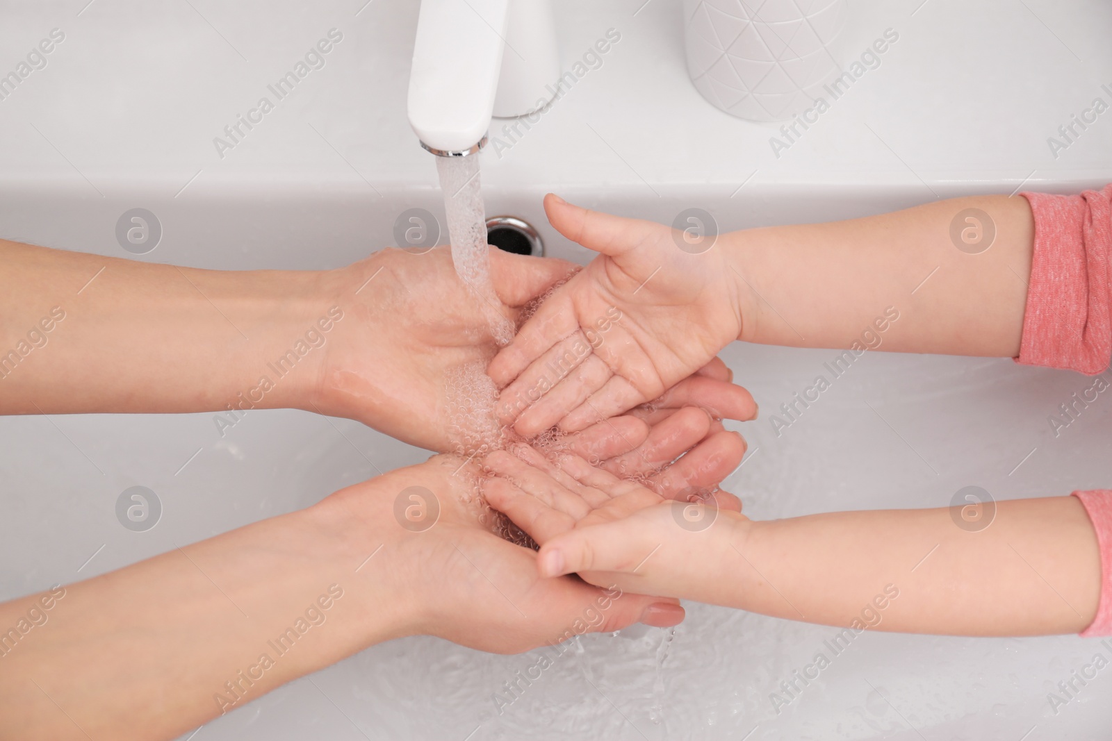 Photo of Mother and daughter washing hands in bathroom at home, closeup