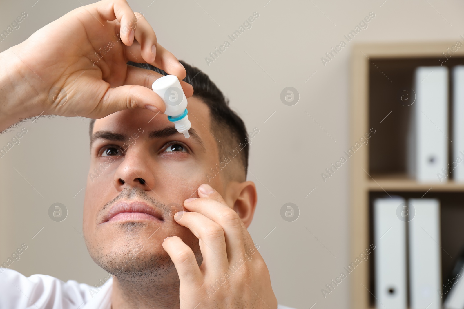 Photo of Man using eye drops in light office