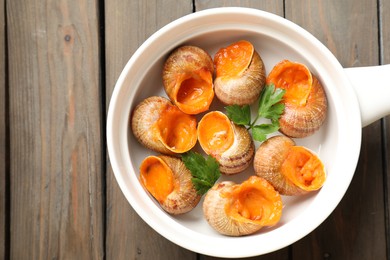 Photo of Delicious cooked snails with parsley on wooden table, top view. Space for text