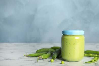 Photo of Baby food in jar and fresh green peas on white marble table against light blue background. Space for text