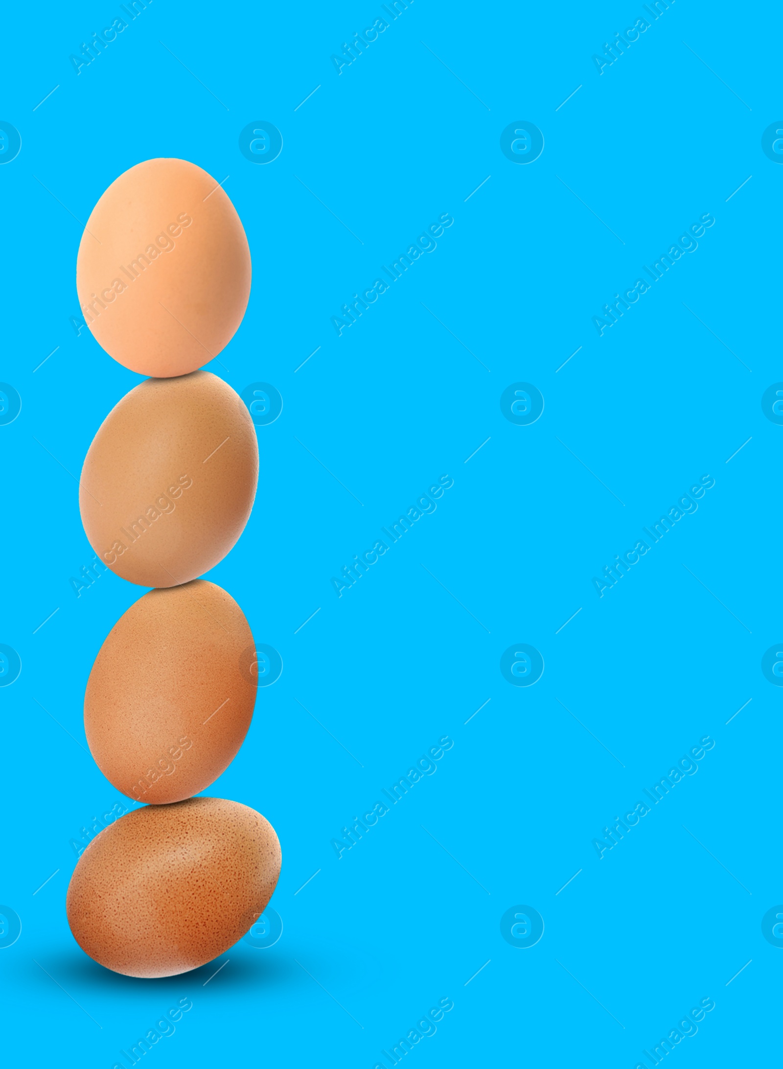 Image of Stacked fresh chicken eggs against light blue background. Space for text