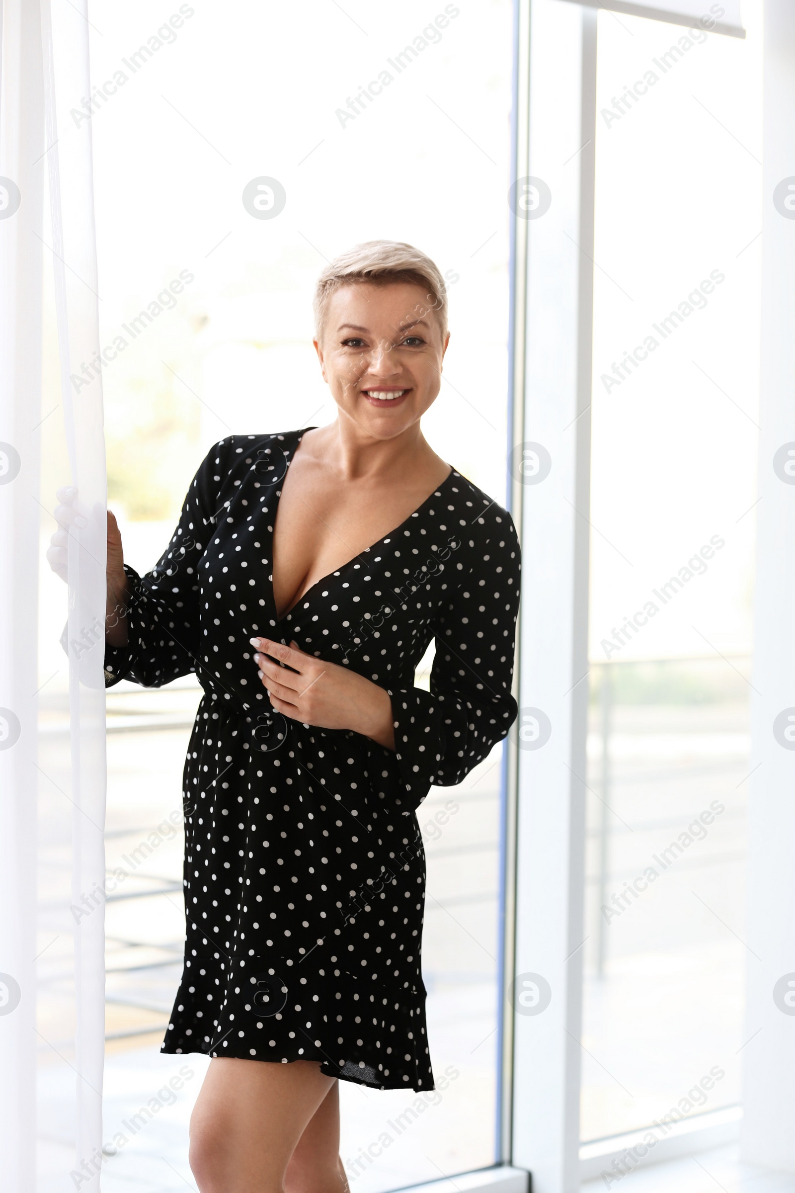 Photo of Beautiful mature woman wearing black dress near window indoors