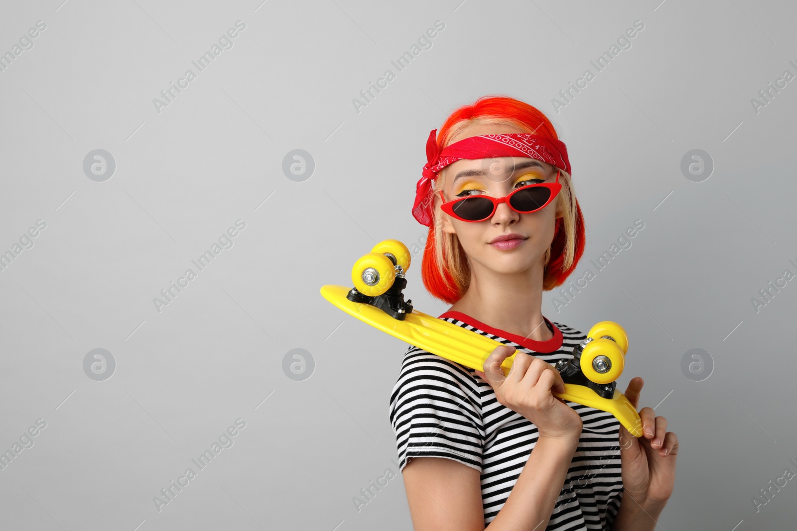 Photo of Beautiful young woman with bright dyed hair holding skateboard on light grey background, space for text