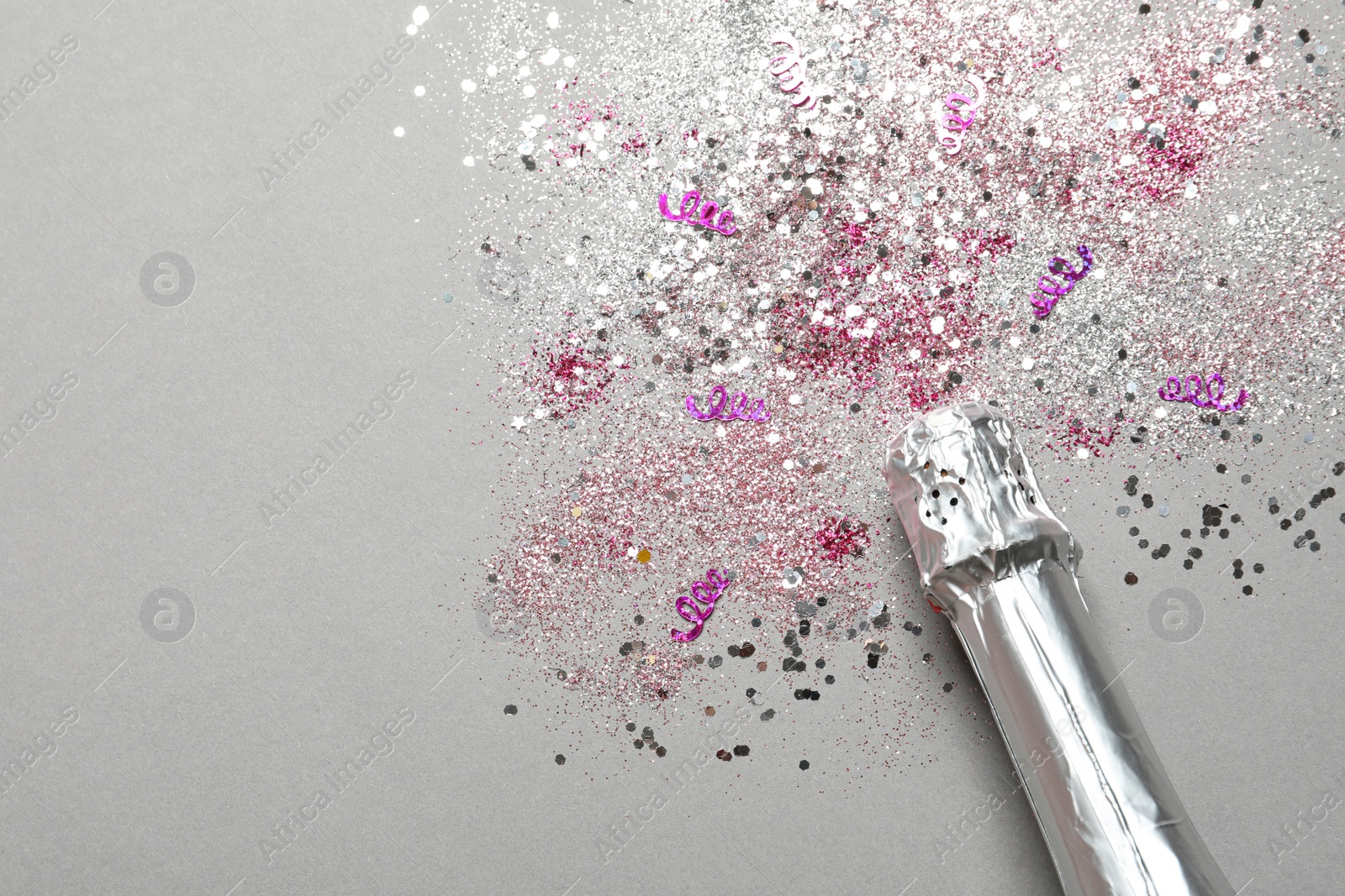 Photo of Bottle of champagne for celebration with glitter and confetti on grey background, top view. Space for text