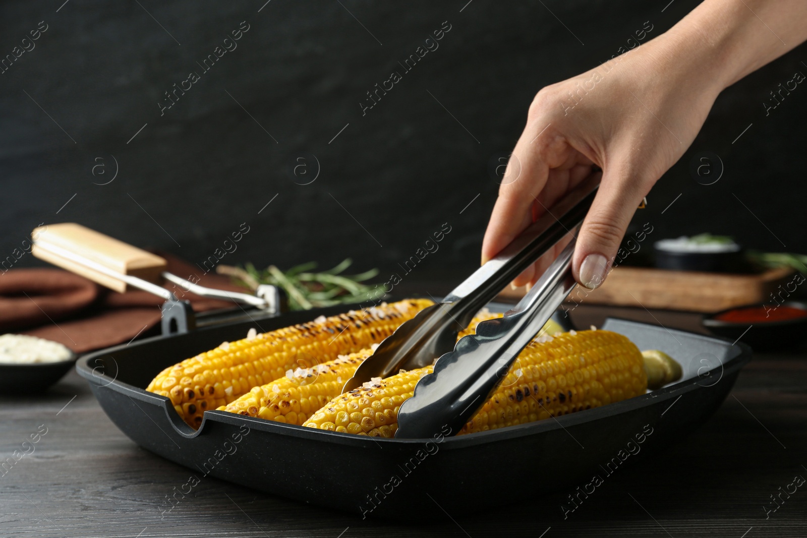 Photo of Woman taking corn with tongs from grill pan, closeup
