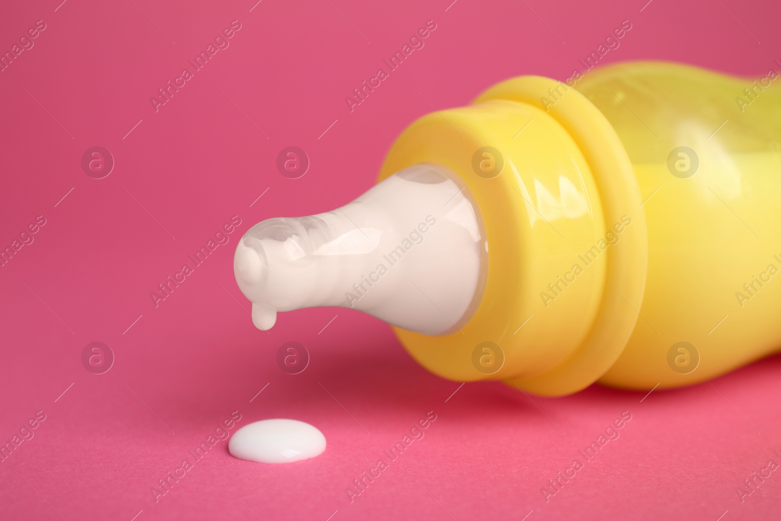 Photo of Feeding bottle with milk on dark pink background, closeup