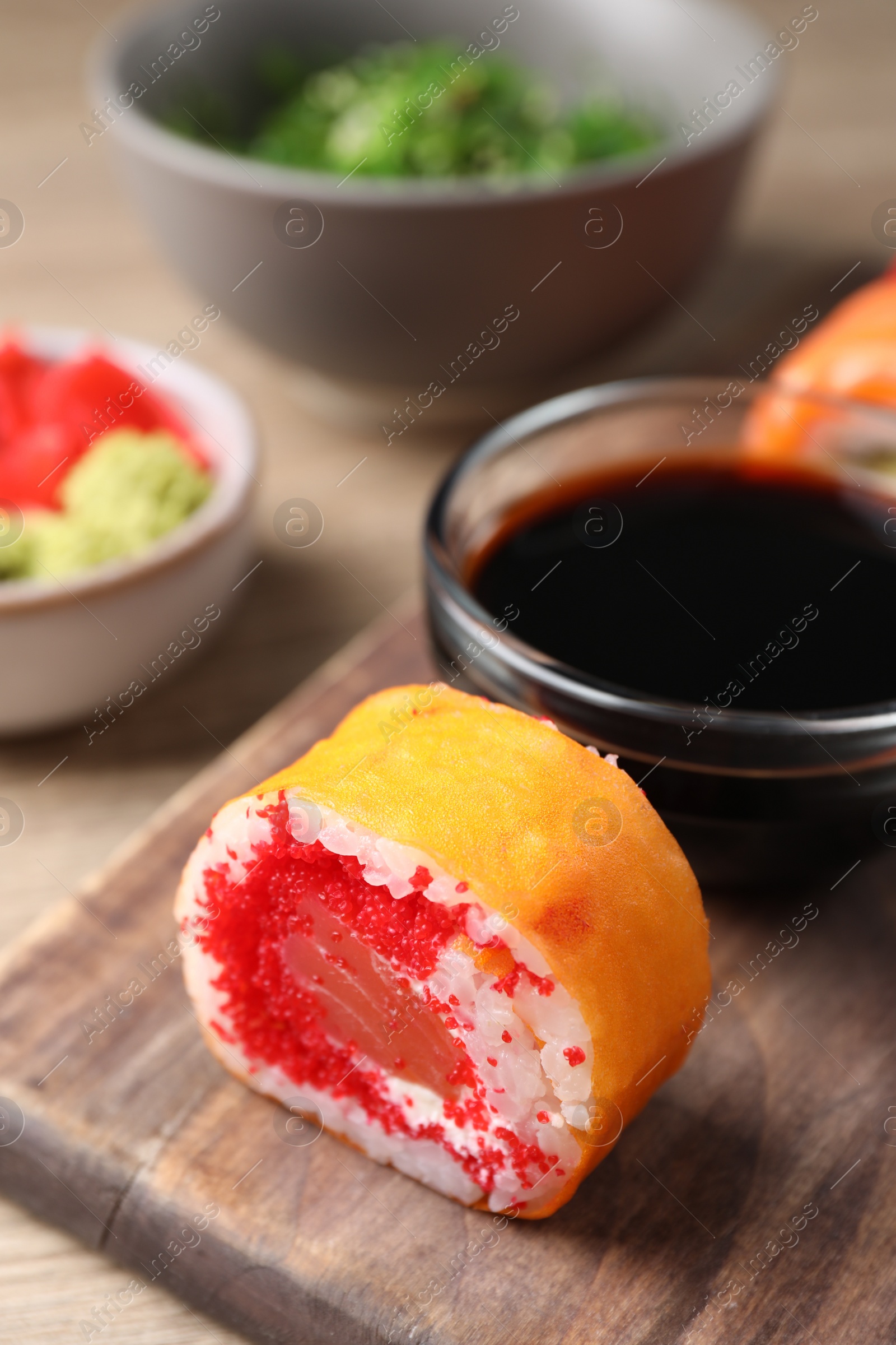 Photo of Delicious sushi roll with salmon and tobiko on wooden board